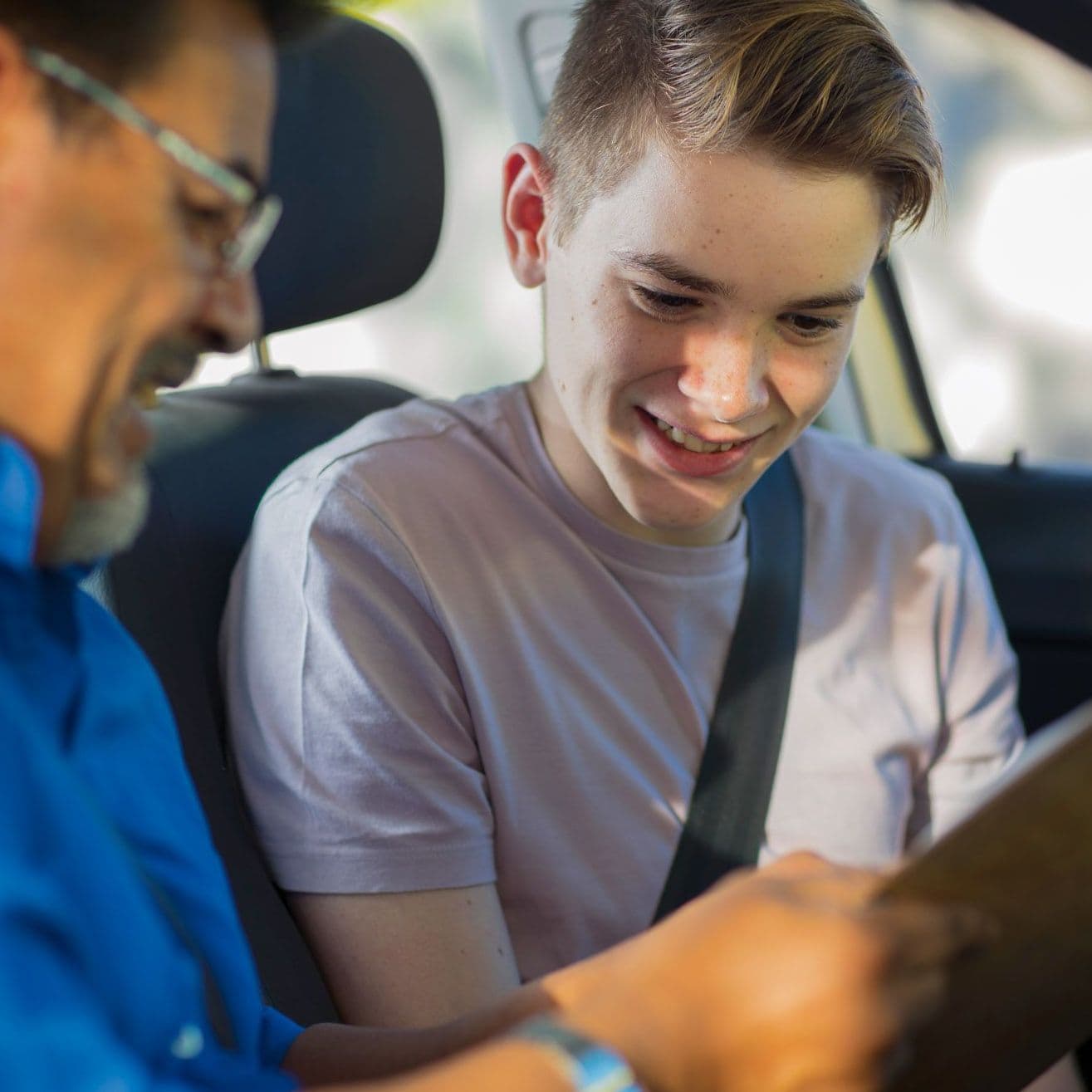 Junger Mann und älterer Mann sitzen im Auto und betrachten ein Clipboard.