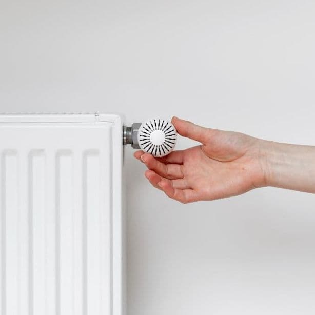 Eine Hand dreht am Heizungsthermostat.