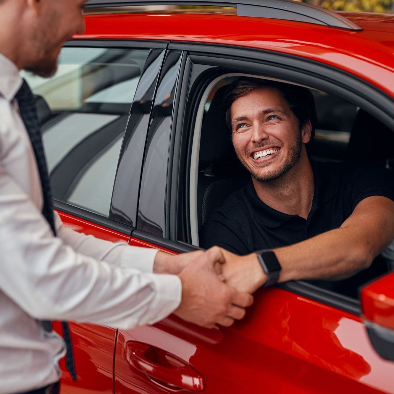 Junger Mann sitzt in einem Auto und reicht einem anderen Mann die Hand.