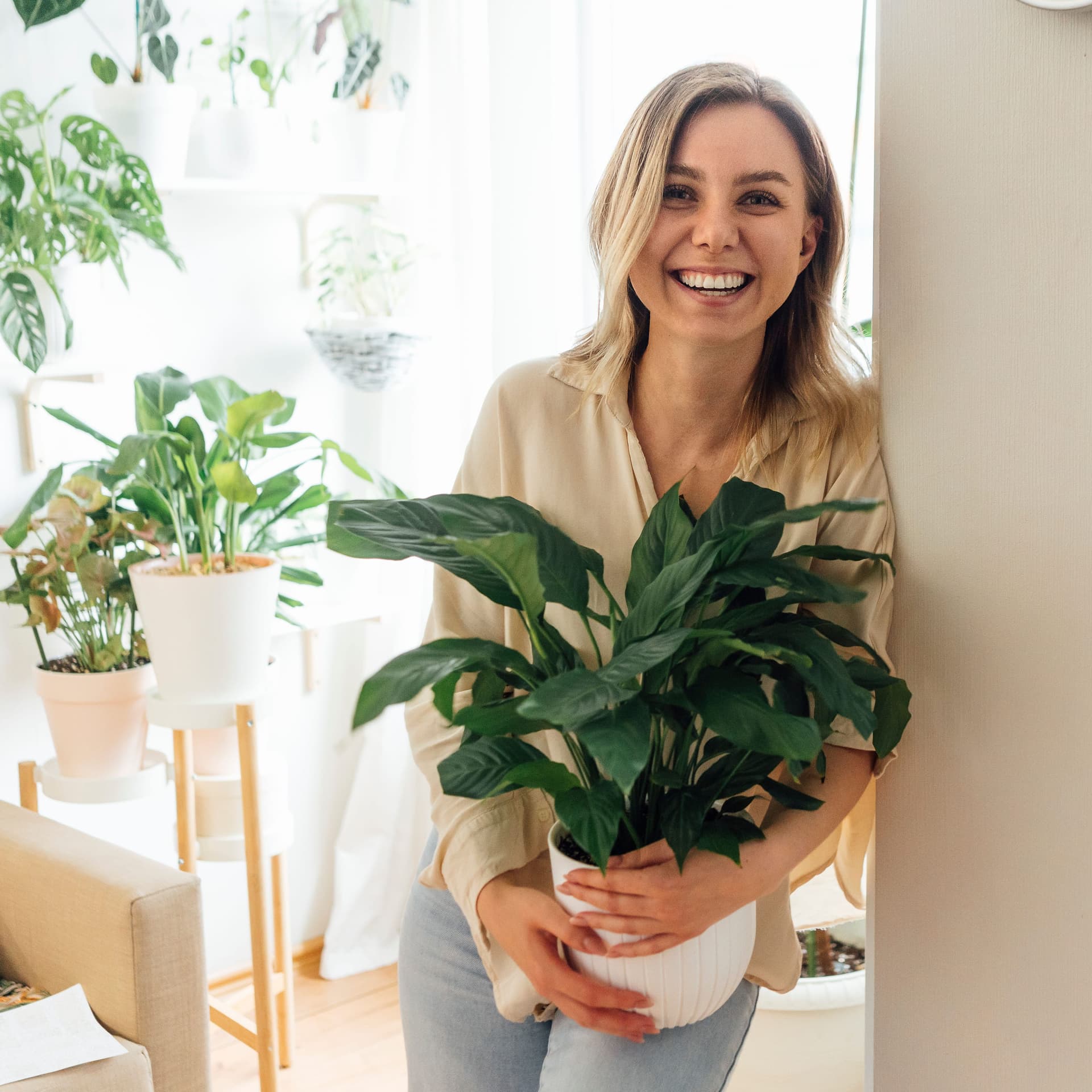 Frau mit Topfpflanze im Arm lehnt an der Wand.