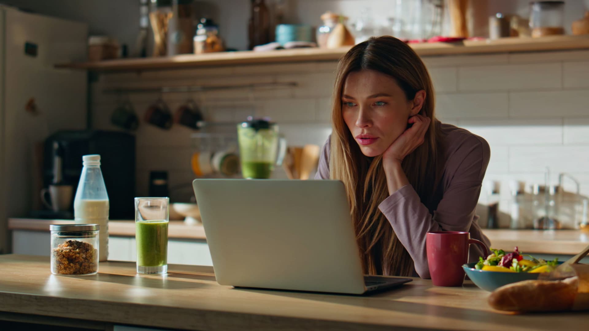 Frau steht in der Küche mit einem Laptop auf der Arbeitsfläche.