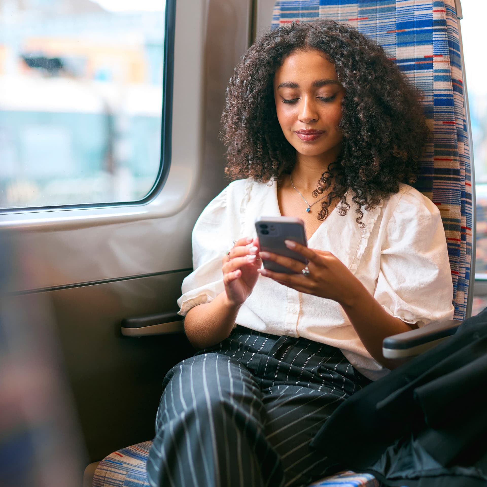Frau sitzt mit Handy im Zug.